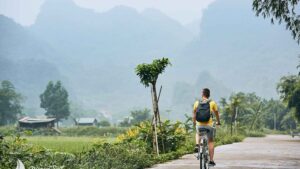 Trip by bike. Man with backpack bicycling on road against karst formation in Ninh Binh province Vietnam